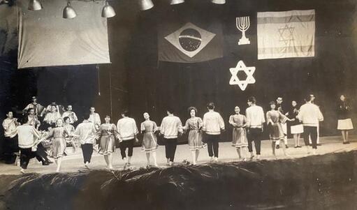 Chinani group's performance at the 2nd Multicoloured Folkloric Festival at Teatro Nacional de Brasília, men and women dancing on stage with Brazil and Israel flags hanging overhead