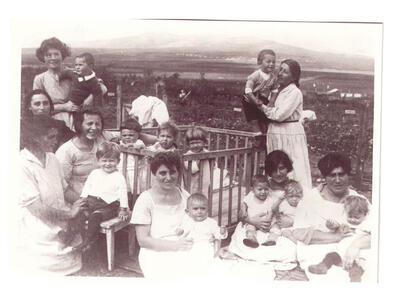 Outdoors, 8 women holding and caring for 10 toddlers, three in a crib