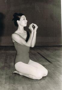 Ruth Eshel kneeling on a stage with her hands cupped in an oval shape