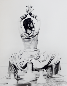 Ze'eva Cohen dancing, squatting low over some pieces of pottery with her wrists crossed above her head