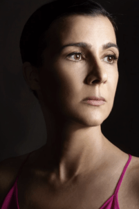 Three-quarter profile of woman against black background, dark hair slicked back, 