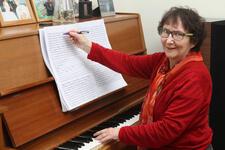 Rachel Galinne in red outfit posed and smiling while at piano adding notation to sheet music