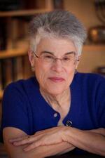 Judith Hauptman wearing a blue top and glasses smiling into the camera with arms crossed over one another