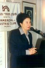 Ora Namir standing in front of a microphone with a sign behind her with Hebrew and English