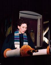 image of a dark-haired woman with a tallit reading Torah