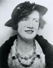black and white photograph of a woman wearing a hat and a dark jacket and a necklance, looking off to the side with a slight smile on her face