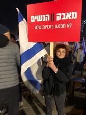 photograph of a woman holding a large red sign with Hebrew writing