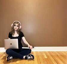 Miriam Anzovin sitting on the floor, wearing headphones, with laptop and book in hand