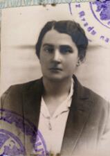 black and white photograph of a woman with dark hair pulled back, looking stoically at the camera, with purple stamp
