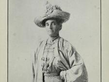 Black and white historical photo of a woman wearing a light colored dress and a large hat, with a serious expression