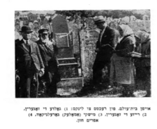 black and white photograph with two women in white head scarves with prayer books and three men in a cemetery