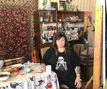 Zoya Cherkassky sitting at a table in a room with china shelves and a Persian rug wall hanging