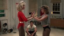 Film still with two women dancing with each other while a man, seated, watches