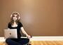 Miriam Anzovin sitting on the floor, wearing headphones, with laptop and book in hand
