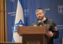 Man with kppah and beard speaks at podicum with Israeli flag in background