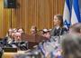 Woman in police uniform speaks at a podium, Israeli flag in background