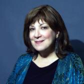 Portrait of Avivah Zornberg looking into camera in front of a blue background photographed by Joan Roth