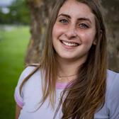 Photo of Ella Plotkin-Oren, in front of a tree wearing a white shirt with pink detailing.