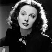 Hedy Lamarr in a long sleeved black dress with a brooch, seen from the chest up in the film The Heavenly Body
