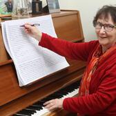 Rachel Galinne in red outfit posed and smiling while at piano adding notation to sheet music