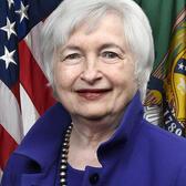 Official portrait of Janet Yellen smiling in a blue jacket and a necklace in front of an American flag