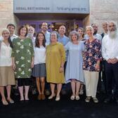 A group of ten men and seven women, smiling and standing in front of a building labeled "Segal Beit Midrash" in English and Hebrew