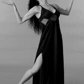 Studio portrait of Susana Weingarten striking a dancing pose, looking up at the ceiling, and wearing a black dress