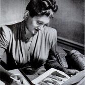 Nettie Rosenstein holding a pencil and looking at a fashion plate featuring four dresses