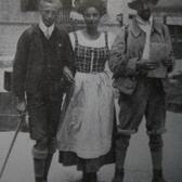 Emmy Eisenberg, arms linked with two men, all wearing boots, stockings, and short pants/a shorter skirt