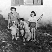 A woman leaning down and holding the hands of a toddler, with a man kneeling beside them and an older girl (Yona Wallach) standing nearby