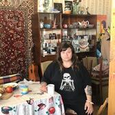 Zoya Cherkassky sitting at a table in a room with china shelves and a Persian rug wall hanging