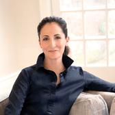 Rabbi Jen Schwarz sits on a sofa, leaning back against the cushions with her arm across the back of the sofa