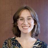 Woman with chin-length brown hair and glasses posing against a dark background