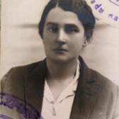 black and white photograph of a woman with dark hair pulled back, looking stoically at the camera, with purple stamp