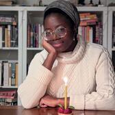 photograph of a Black woman with a head scarf in front of a raspberry tart with a candle