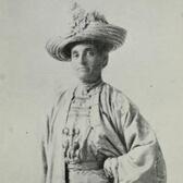 Black and white historical photo of a woman wearing a light colored dress and a large hat, with a serious expression