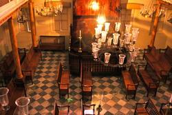 High-angle view of a room with a natural wooden Torah ark and benches, chandeliers, and checkered floor tiles