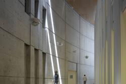 A curved hallway of simple grey stone, with very high ceilings and skylights