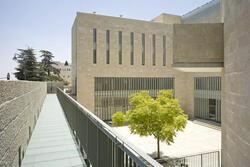 A minimalist building of tan stone, with a small courtyard and a tree
