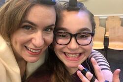 Ma'ayan Rosenbaum, holding up a hand to show the straps of her tefillin, with her mother standing beside her with an arm around her shoulders, wearing tefillin, tallit, and kippah
