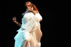Minalu Degia dancing on stage, wearing a voluminous dress of crimped white cloth