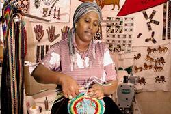 A woman weaving, sitting in a tent with other woven objects and patterns hung around her