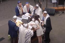 Annie Katz reading Torah at the Bimah surrounded by 6 men