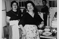 Black and white photo of three women laughing in a kitchen