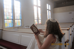 Emerson wearing her kippah, reading her book in a church. 