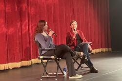 Judith and Ma'ayan Rosenbaum sitting on a stage with microphones, red curtain behind them