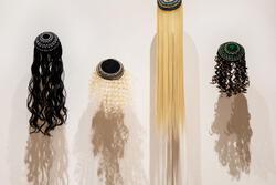 Installation of four kippot with hair coming out against a white wall