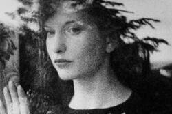 Black and white photograph of woman looking out a window with her hand against the glass.