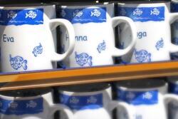 souvenir name mugs featuring illustrated fish. Names "Eva" and "Hanna" are on the mug.