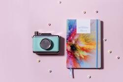 Image of a Journal and a Camera next to each other. Pink background.